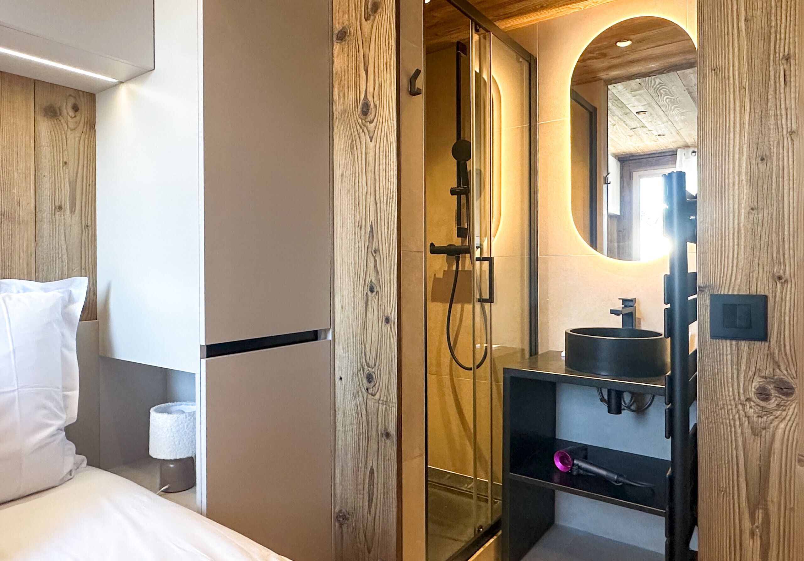 A modern bathroom with a glass shower enclosure, a wooden vanity with a black sink, and a mirror with an oval frame.