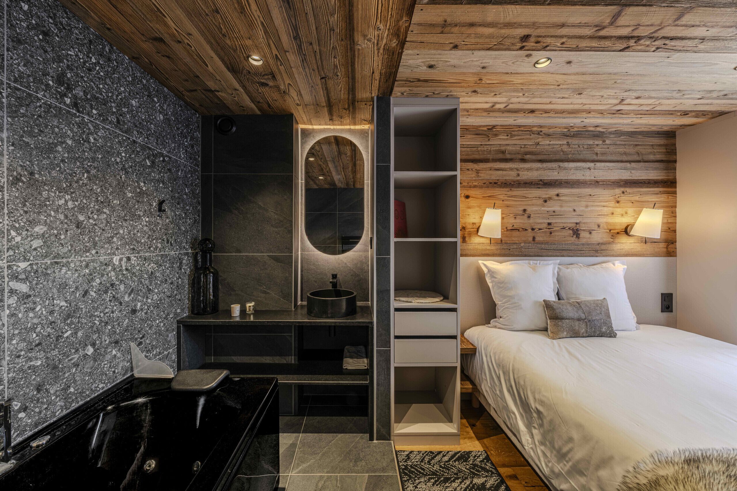 Un dormitorio moderno con techo de madera, una cama grande con ropa blanca, una estantería empotrada y una bañera negra.