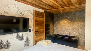 Et soveværelse med træloft, et ophængt fjernsyn, en stenvæg og et spa-område med jacuzzi.