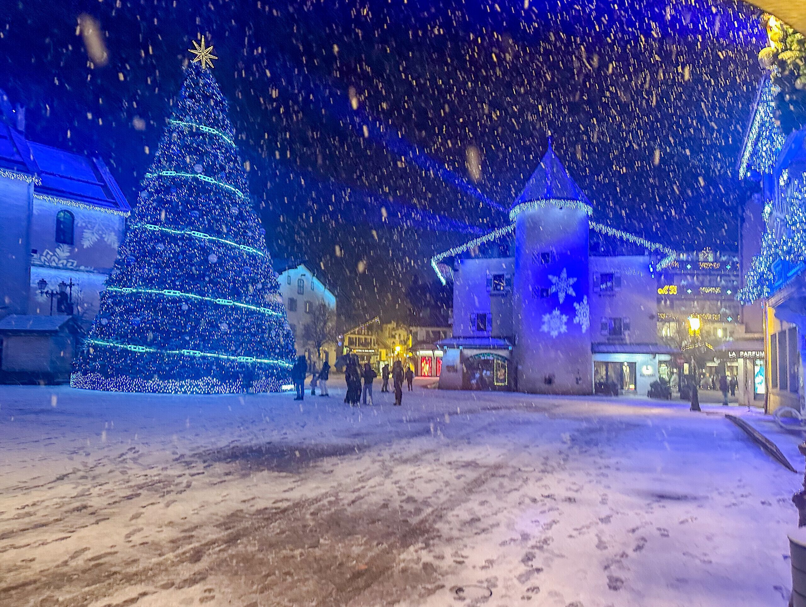 A snow-covered square with a large illuminated Christmas tree and a castle-like structure.