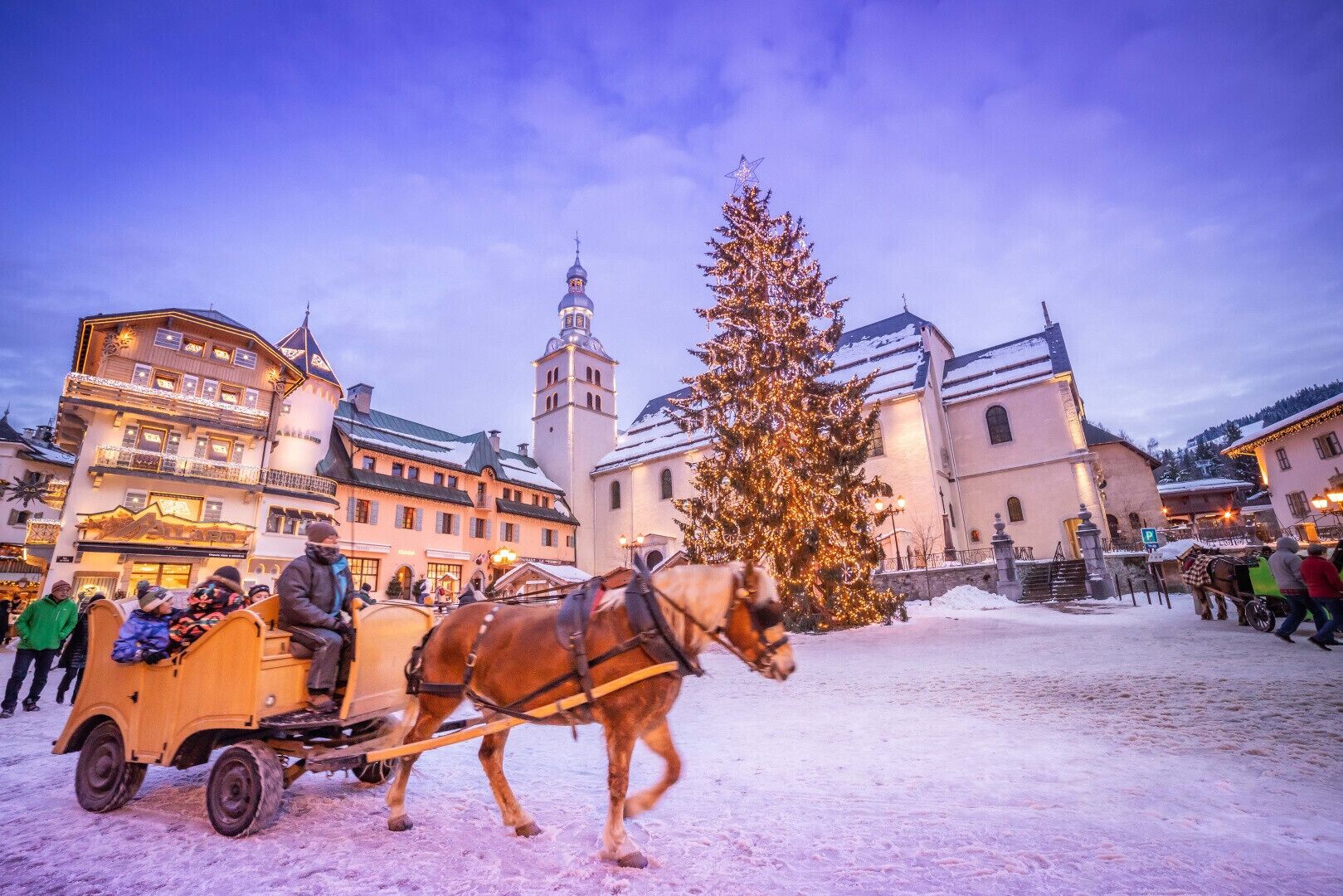 En hästdragen vagn på ett snötäckt torg med byggnader i bakgrunden.