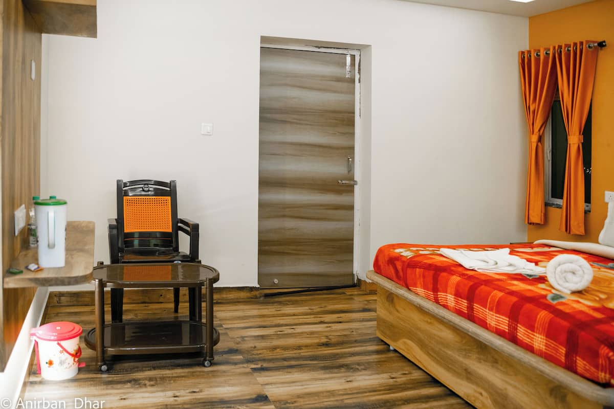 Quarto de hotel com piso de madeira, uma cama com manta vermelha, uma mesa pequena com uma cadeira, micro-ondas e uma porta com espelho.