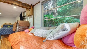 Ein Schlafzimmer mit einem großen Bett, einem hölzernen Kopfteil, einem Fenster mit Blick auf Grünflächen und einem Holzbalken an der Decke.