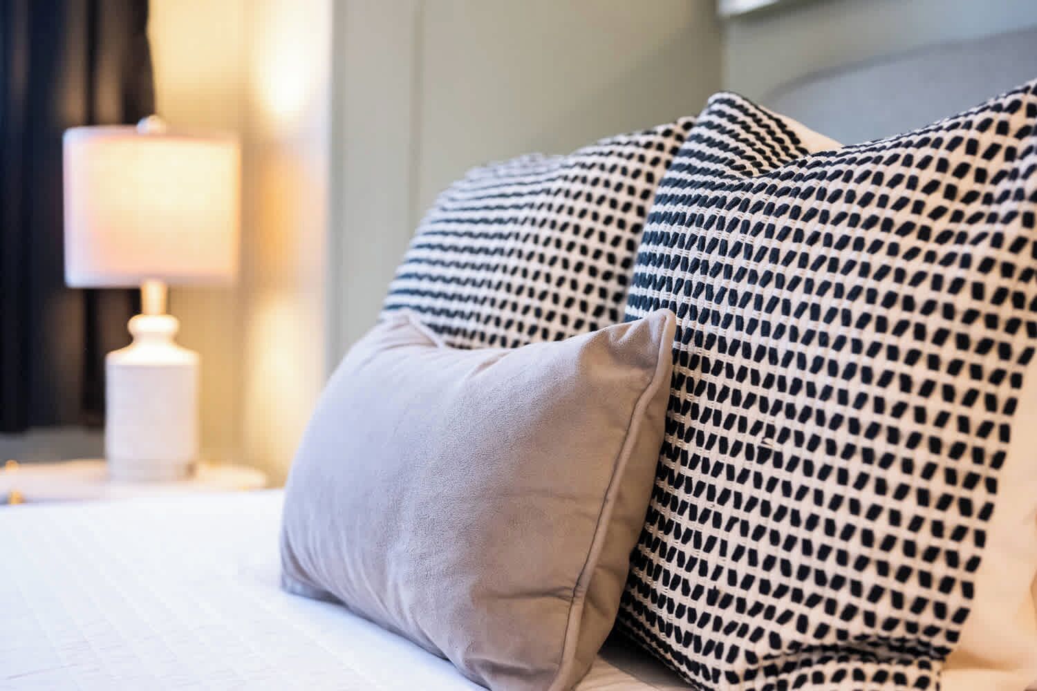 A bed with two pillows, one plain and one patterned, and a bedside lamp.