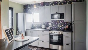 A modern kitchen with grey cabinets, a stainless steel stove, a microwave, and a black countertop. - Tiny Home fit for a King: Near Belmont Park! (Dayton)