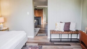 A hotel room with a bed, a bench with cushions, a lamp, and a view into the kitchen area. - Tiny Home fit for a King: Near Belmont Park! (Dayton)