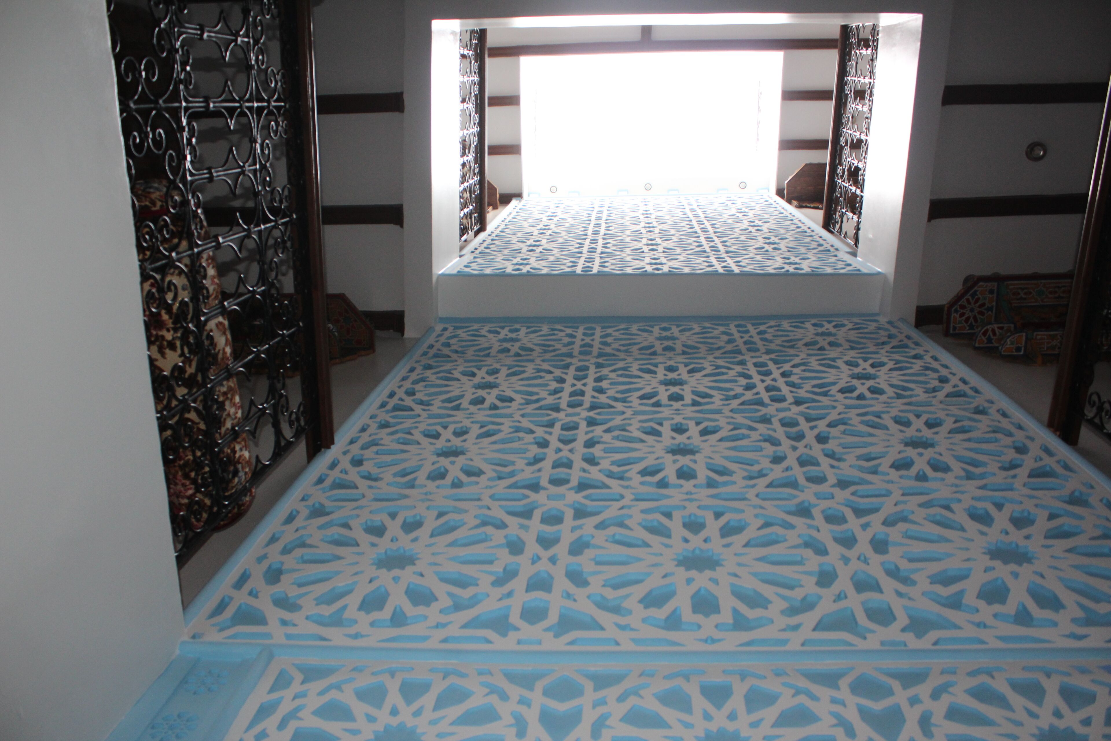 Une pièce avec un sol à motifs, une grille métallique et une vue par la fenêtre.