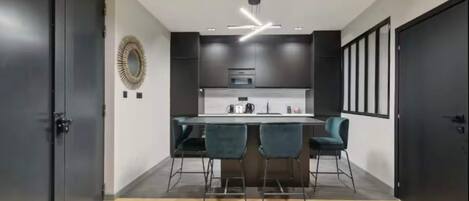 A modern kitchen with a central island, dark cabinetry, and a ceiling light fixture.