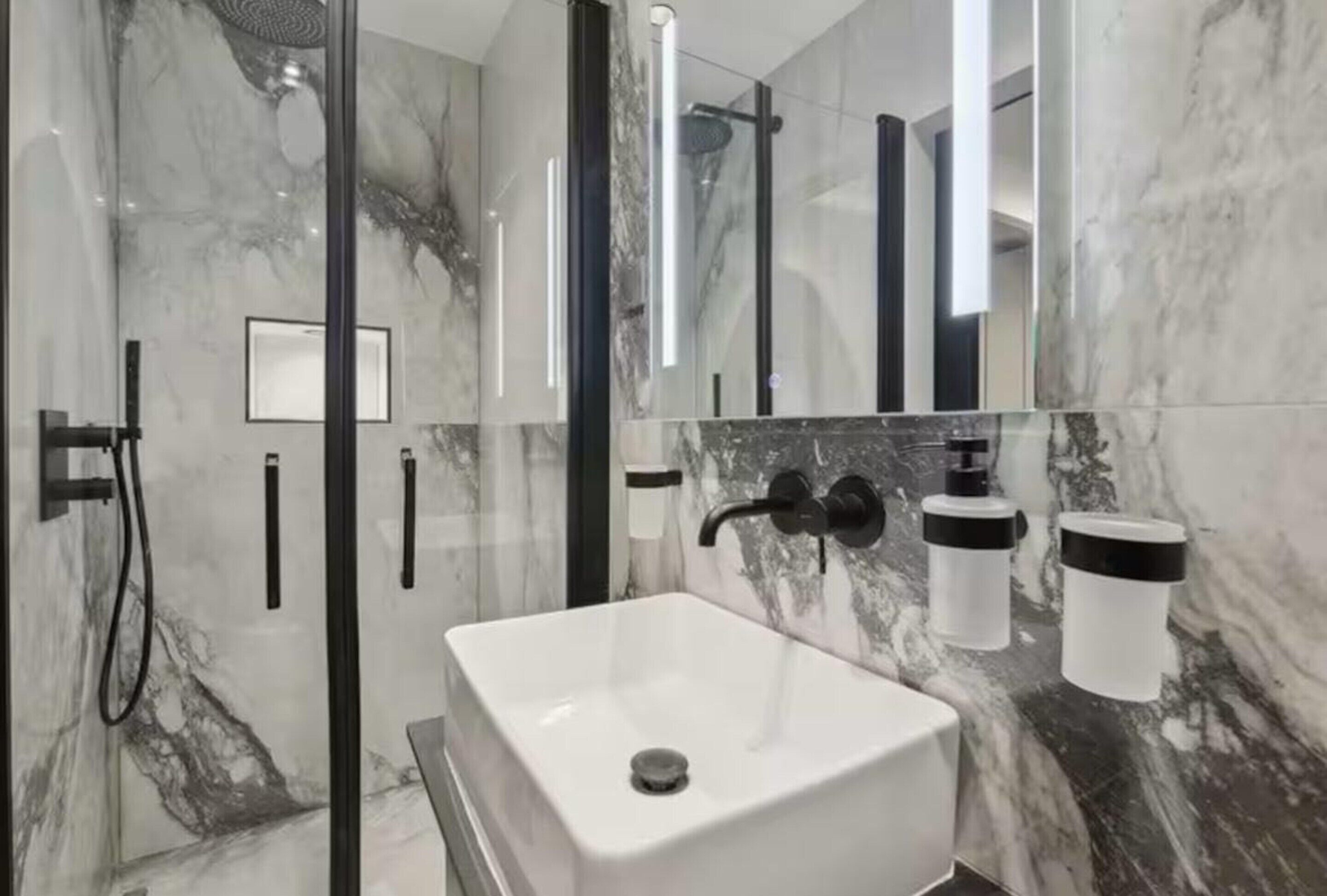 Un baño moderno con ducha de vidrio, un lavamanos blanco y paredes de mármol.