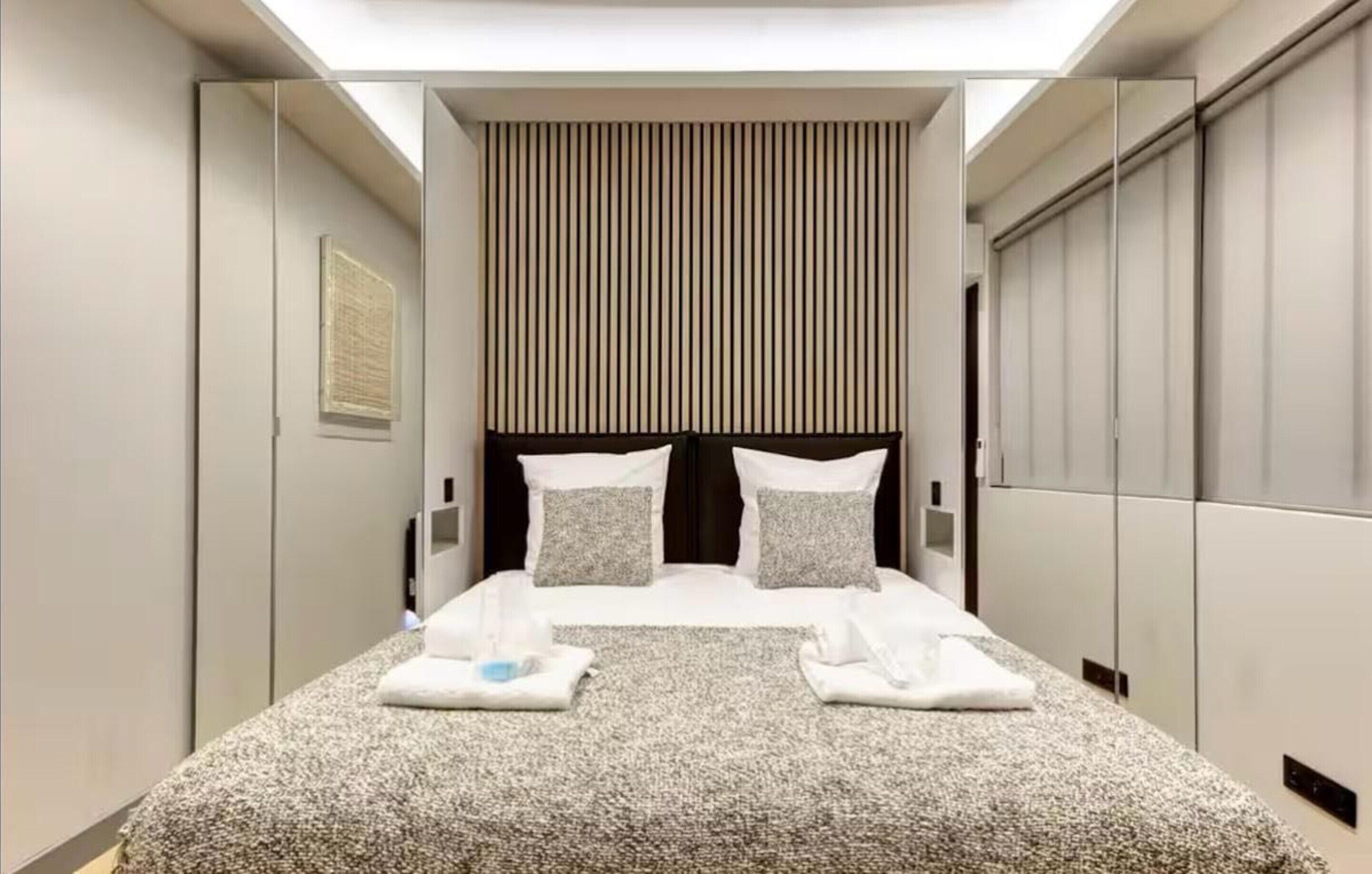 Una habitación de hotel moderna con una cama grande, un muro de espejo y un cabecero a rayas.