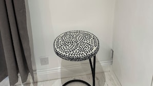 Una mesita pequeña, redonda, con un diseño blanco y negro y una pata metálica negra, ubicada frente a una pared blanca con un espejo de marco plateado arriba.
