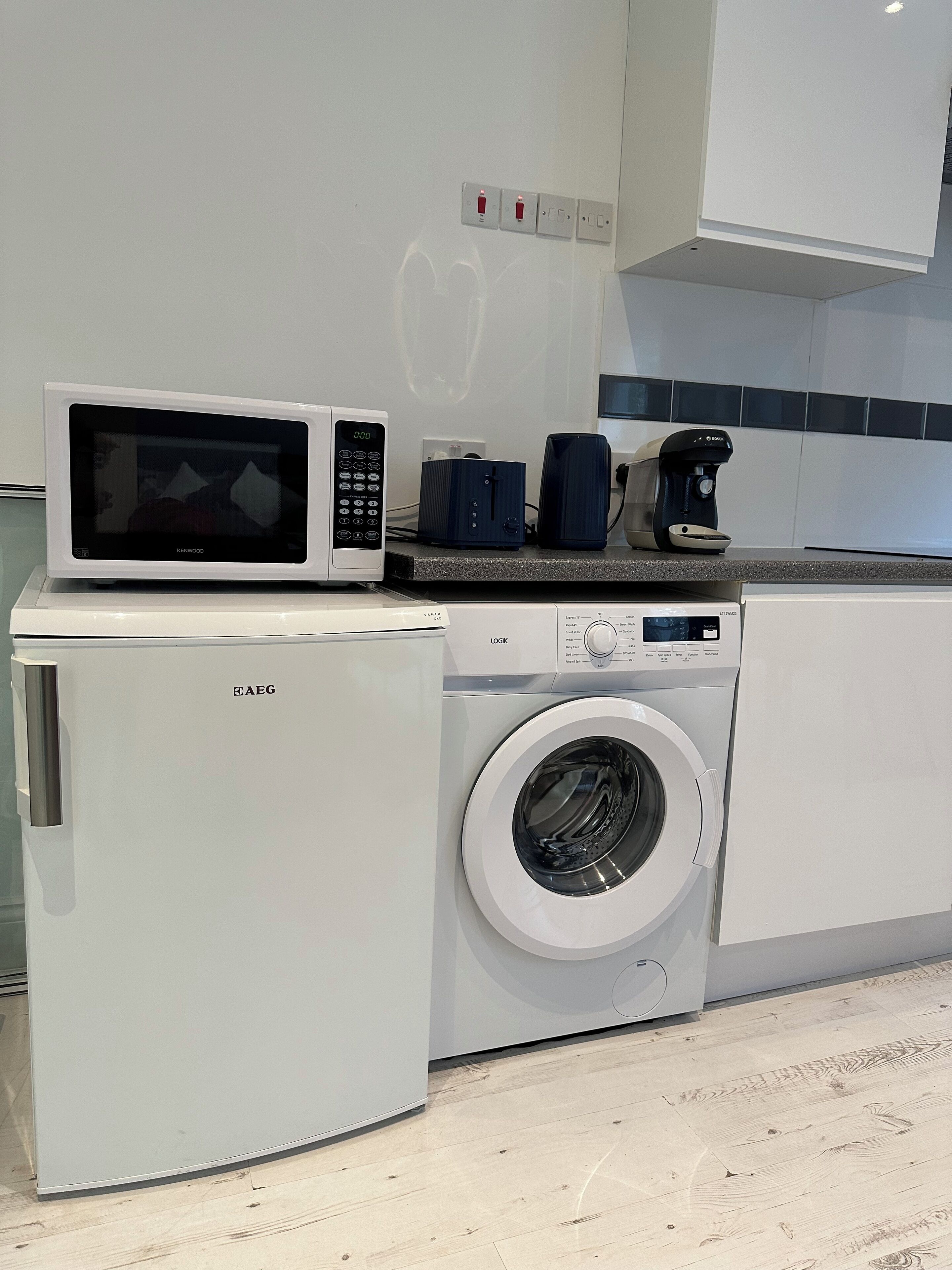 Une cuisine compacte équipée d’un four à micro-ondes, d’une machine à café et d’un lave-linge.