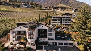 A modern hotel with multiple floors, a swimming pool, and a view of the surrounding mountainous landscape. - Apartment with large south-facing terrace, incl. garage parking space (Dorf Tirol)