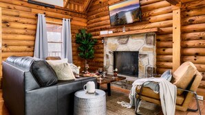 L’intérieur chaleureux d’un chalet en bois avec une chemin ée en pierre, un canapé en cuir et un téléviseur à écran plat fixé au-dessus de la cheminée.