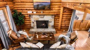 L’intérieur d’un chalet confortable, avec des murs en rondins de bois, une cheminée en pierre, des canapés en cuir et un téléviseur fixé au mur.