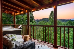 Une terrasse en bois avec un jacuzzi, un coin salon et un verre de vin.