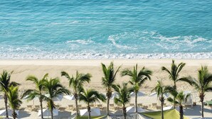 Una playa con palmeras y sombrillas blancas.
