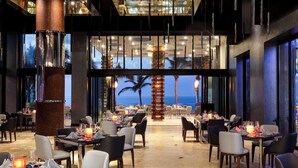 Un restaurante amplio con mesas dispuestas para comer, ventanas grandes que ofrecen vistas al océano y un diseño de interiores moderno.