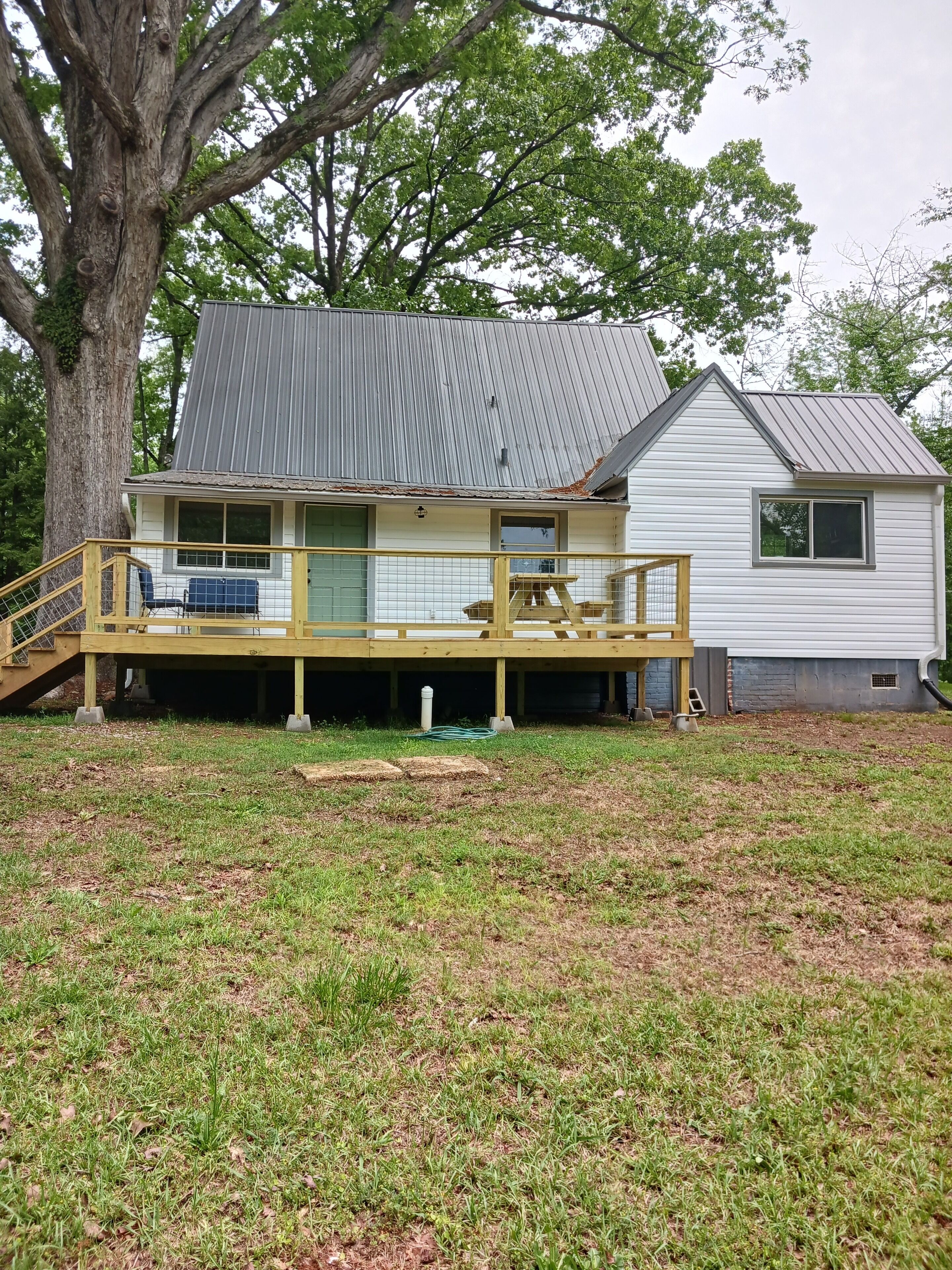 A two-story house with a wooden deck, a metal roof, and a large tree in the background.