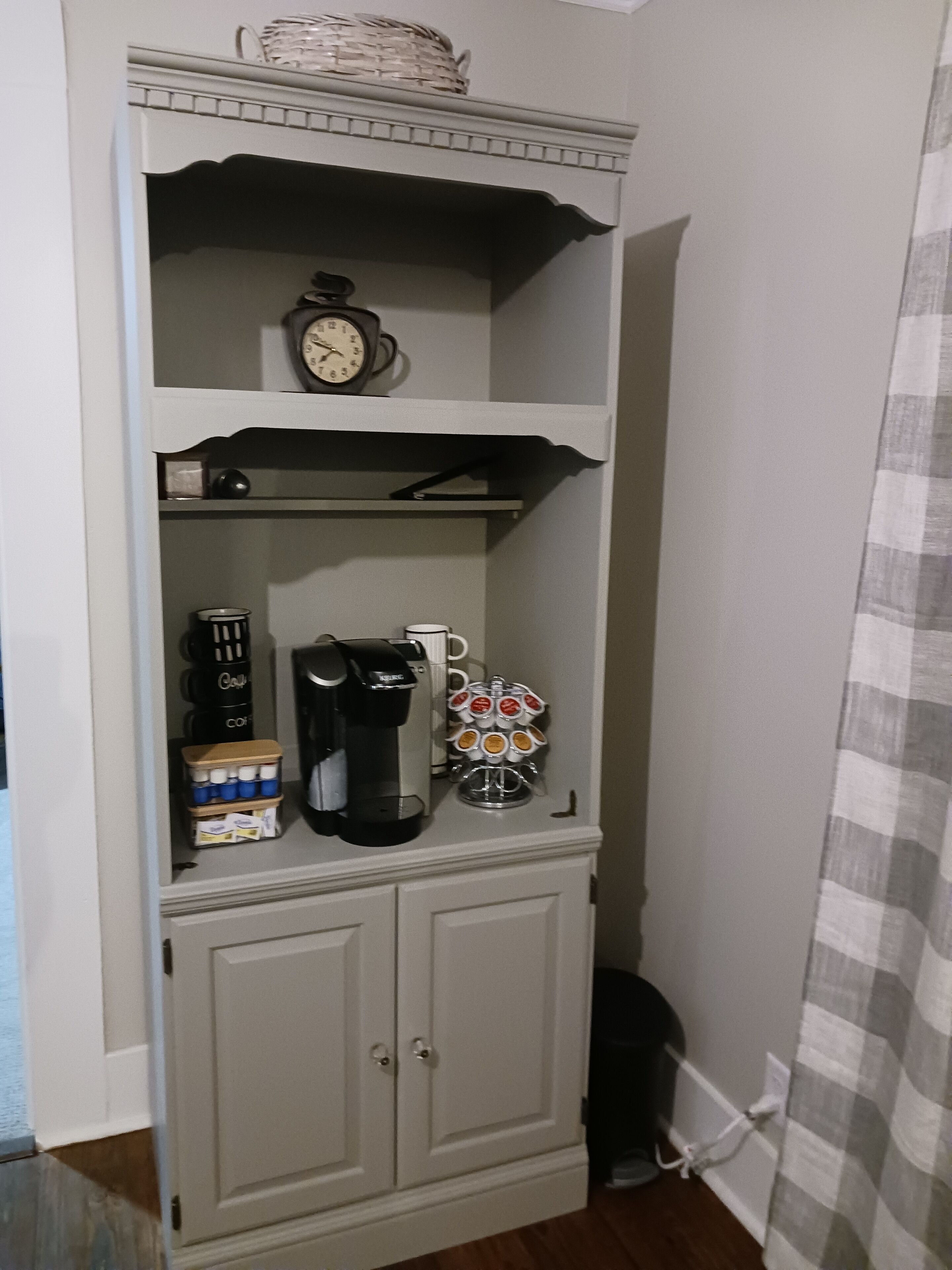 Une cuisine équipée d’une machine à café, d’une horloge et d’un panier placé sur l’étagère supérieure.