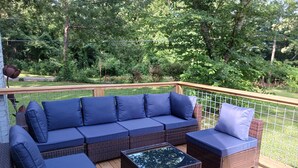 Una terraza con un sofá de mimbre oscuro y dos sillones a juego, una mesita y una barandilla de madera.