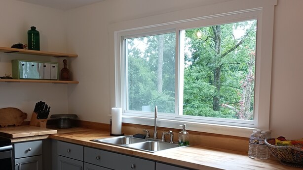 Una cocina moderna con armarios grises, una encimera de madera y ventana con vistas a un bosque.