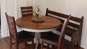 Un comedor con una mesa redonda de madera rodeada por cuatro sillas, un florero con flores y un cuadro en la pared.