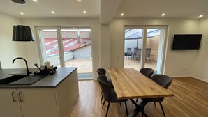 Une cuisine moderne avec un évier, une table à manger en bois et des chaises. Une grande fenêtre offre une vue sur un bâtiment dont le toit est rouge.