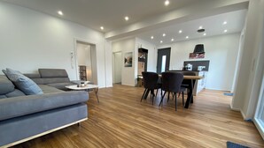 Un salon moderne avec un canapé gris, une table à manger avec des chaises, un plancher en bois et un éclairage encastré au plafond.