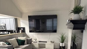 A modern living room with a grey sofa, a white entertainment unit, and a flat-screen TV mounted on the wall. - Modern 2BR,2BA Retreat near AT&T Stadium, Six Flags & Epic Waters, globe  (Arlington)