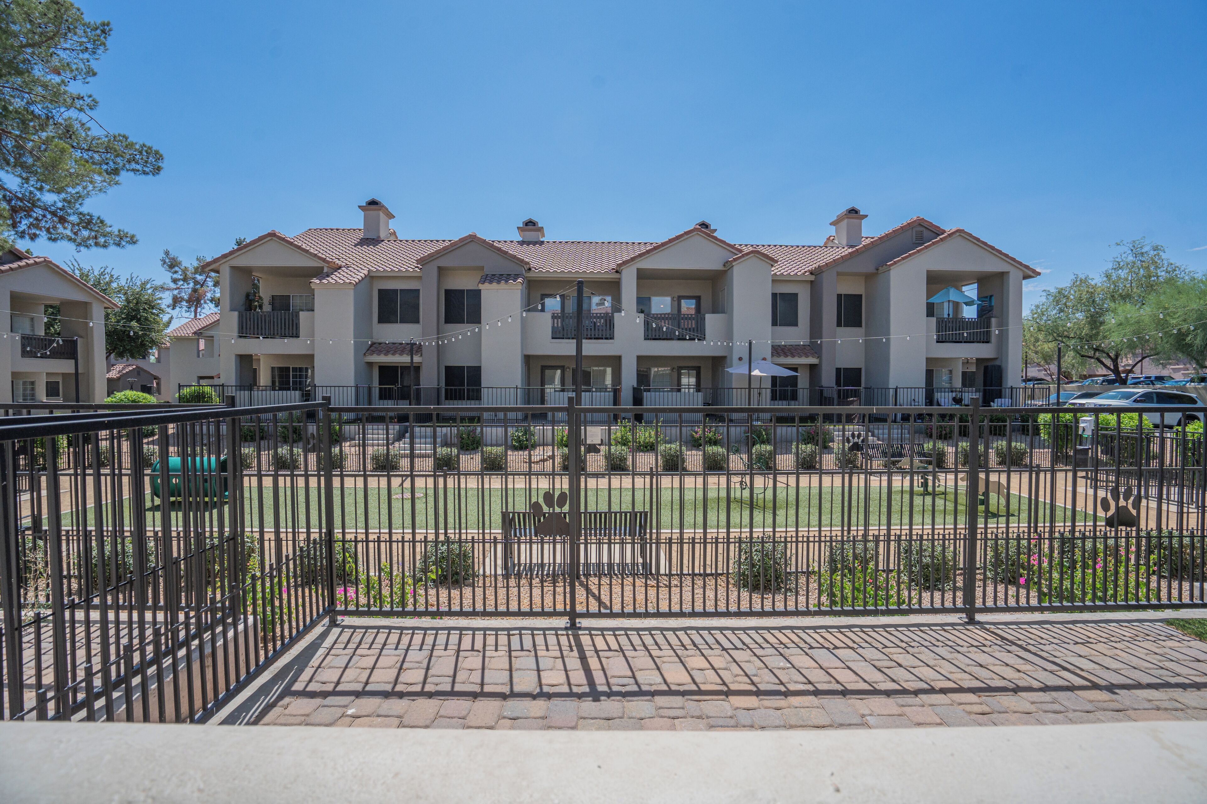 A multi-story residential building with balconies, a fenced courtyard, and a clear blue sky.