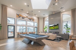 Uma sala de estar moderna com mesa de bilhar, assentos confortáveis, janelas amplas e uma TV de tela plana.