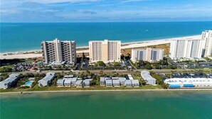 Uma área costeira com um hotel, vários edifícios altos, uma praia e um porto de iates.