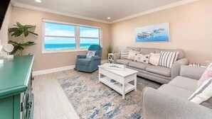 Uma sala de estar com vista para o oceano, um sofá, uma mesa de centro e um armário verde-água.