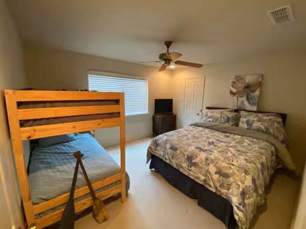 A bedroom with a bunk bed, a flat-screen TV, a ceiling fan, and a bed with floral bedding.