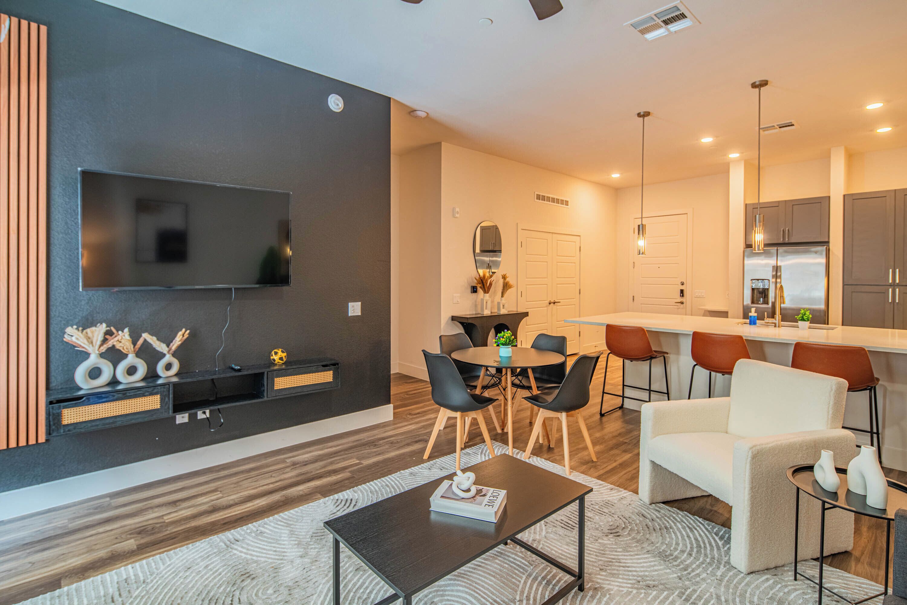Sala de estar moderna com televisão de tela plana, mesa de centro e área de jantar com cadeiras e mesa.