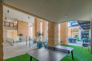 Un patio interior con mesa de ping pong, barandillas de vidrio, pilares de piedra y zonas de estar al aire libre.