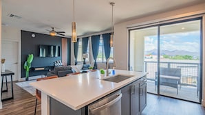 Eine moderne Küche mit Kochinsel, ein Essbereich mit Sofa und Sesseln, ein Flachbildfernseher an der Wand und ein Balkon mit Bergblick.