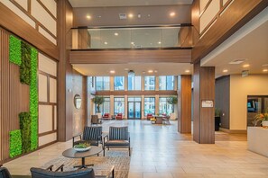 A spacious lobby with a high ceiling, wooden paneling, and a green vertical garden. There are multiple seating areas with chairs and tables, and a reception desk is visible in the background. - ROVE LIVING/KB - Scottsdale Grand (Scottsdale)