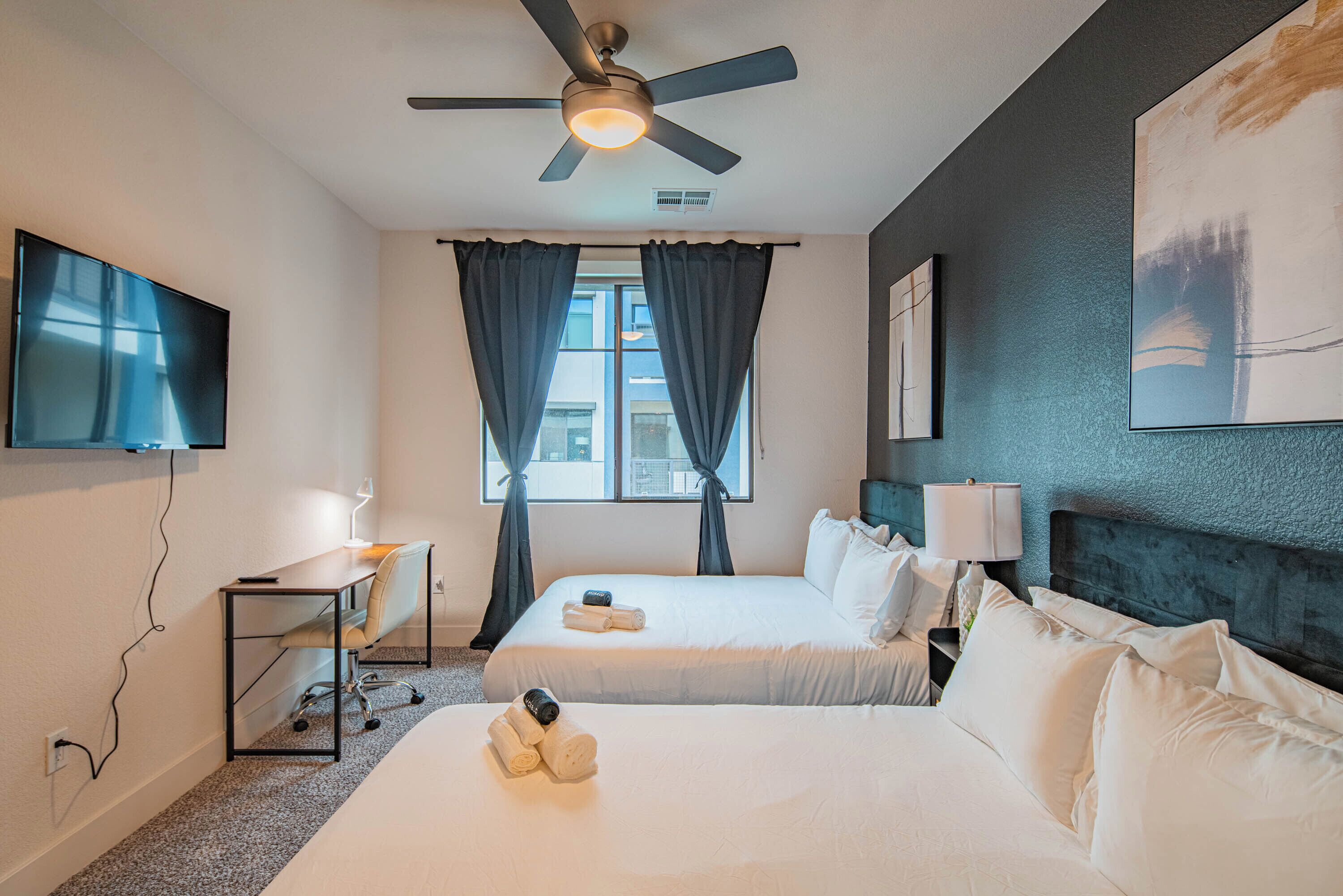 Une chambre d’hôtel avec deux lits, un bureau, une télévision et un ventilateur de plafond.