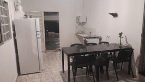 Una cucina compatta con frigorifero, fornello e lavandino. È presente un tavolo da pranzo con sedie.