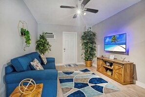 Ein Wohnzimmer mit einem blauen Sofa, einem Holzschrank und einem großen Fernseher an der Wand.