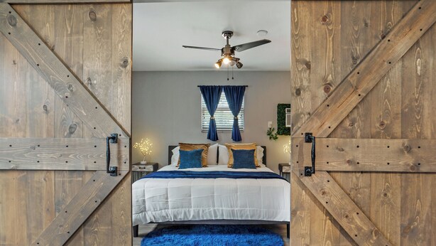 Un dormitorio con cama, cortinas azules, ventilador de techo y paredes de madera.