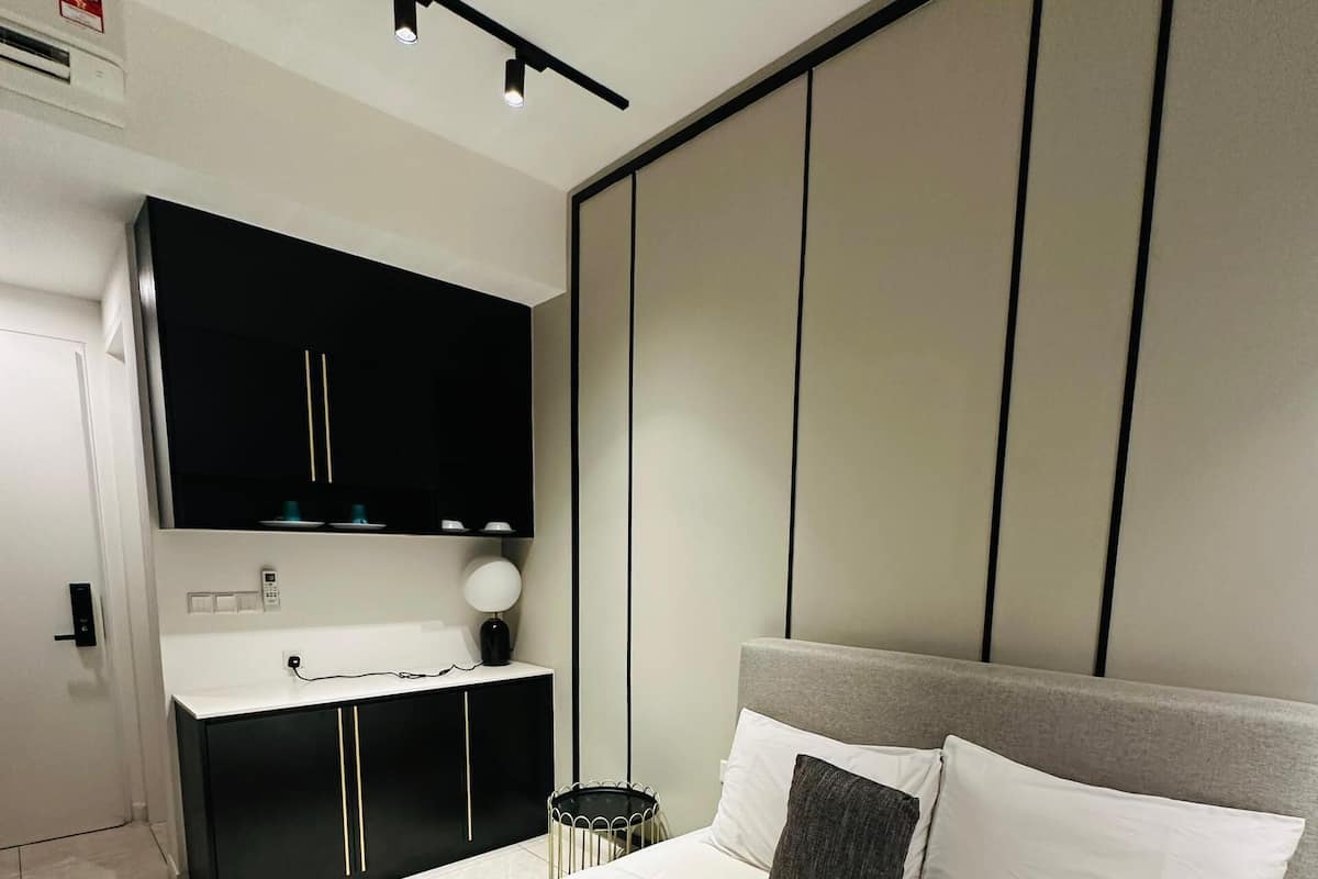 A modern hotel room with a large bed, a bedside table, a black wardrobe, and a small bedside table with a lamp.