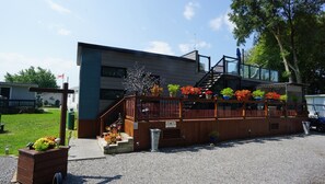 Enjoy a welcoming atmosphere on the deck with potted plants and flowers, surrounded by a grassy lawn and a driveway.