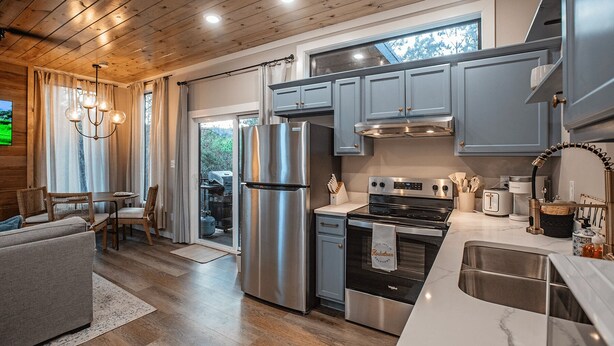 A modern kitchen with stainless steel appliances, grey cabinets, and a large window.