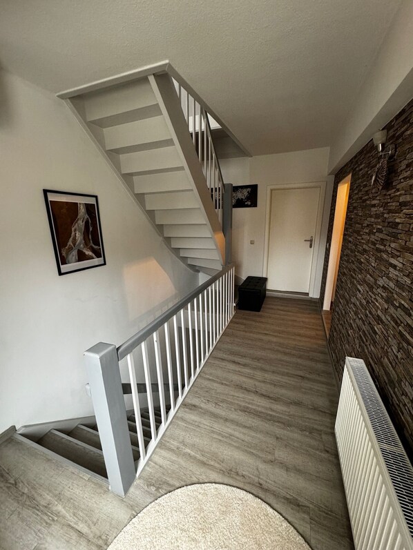A modern staircase with a white railing, a wooden floor, and a stone wall.