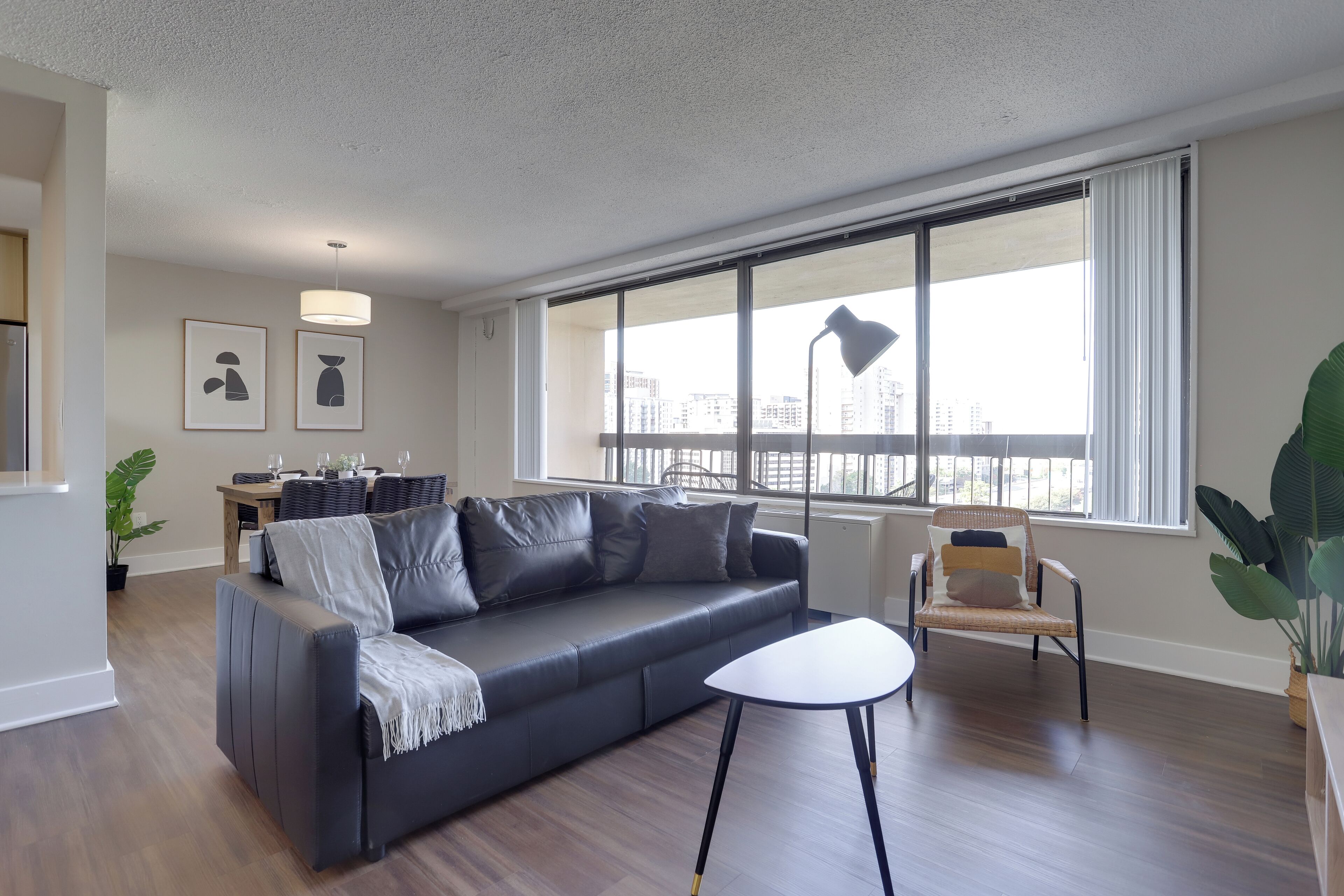 A modern living room with a dark leather sofa, a white coffee table, and a large window offering a city view.