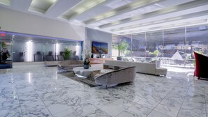 Un vestíbulo espacioso con piso de mármol, muebles modernos y ventanas amplias que ofrecen vistas de la ciudad.