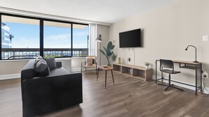 Una sala de estar moderna con un sofá negro, un escritorio de madera, una silla y un televisor montado en la pared.